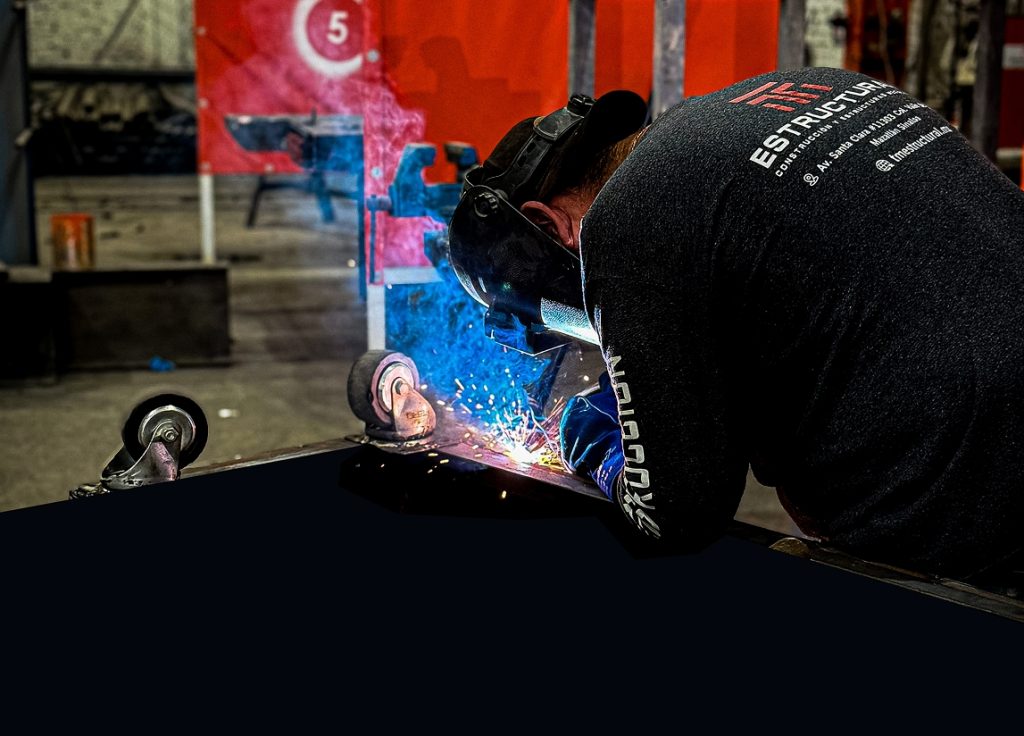 Técnico soldador de TM ESTRUCTURAL trabajando en taller industrial, con chispas azules durante la unión de piezas metálicas.